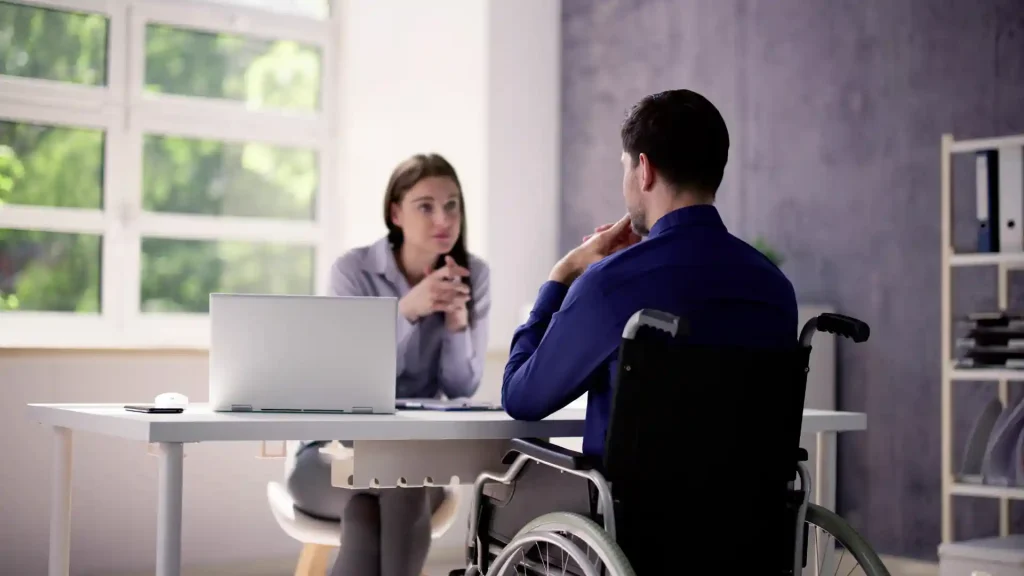 Man in a wheelchair consulting with a woman at a desk.