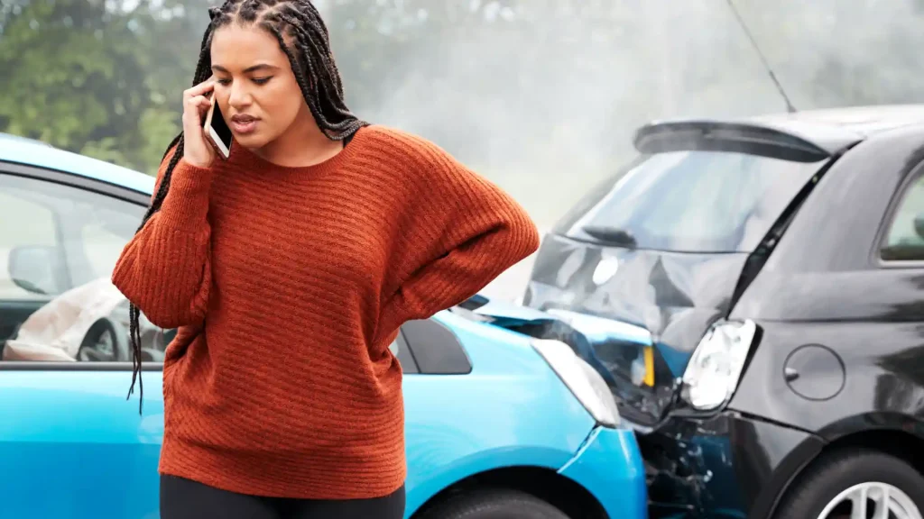 Woman on phone standing near a car accident with smoke.