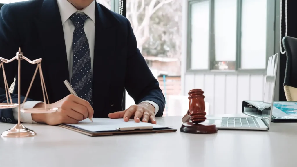 Lawyer in suit writing on clipboard next to gavel on desk.
