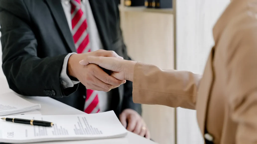 Client and professional shaking hands over legal documents.