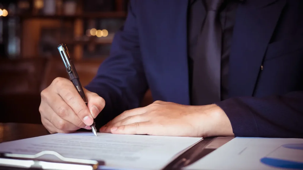 Person in suit signing legal document at desk.