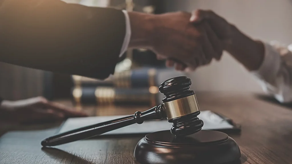 Close-up of gavel with two people shaking hands in background.