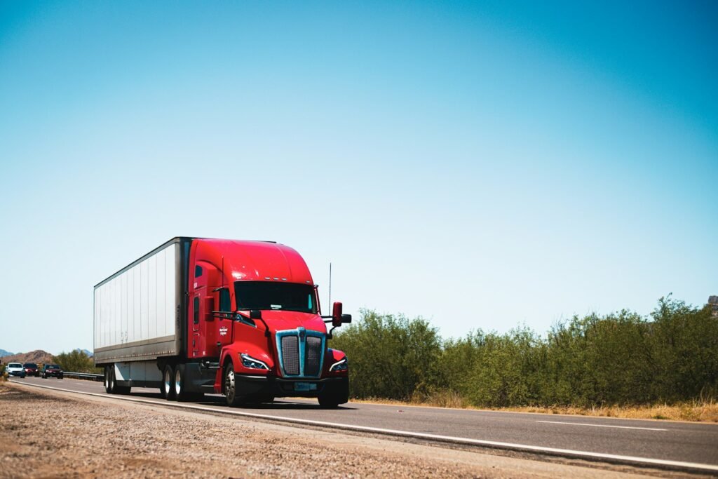 Red semi truck driving down a rural highway