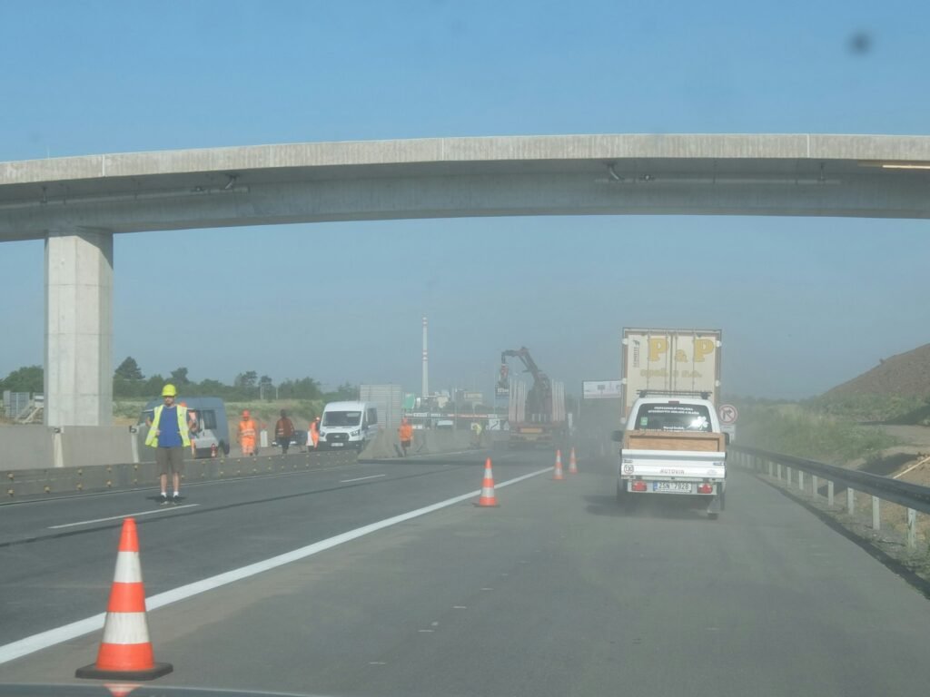 Highway work zone with traffic cones, a worker, and a truck under an overpass